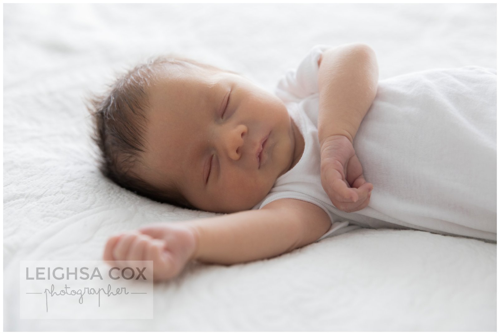 Portrait of newborn baby sleeping peacefully in swaddle surrounded by soft light fabric.