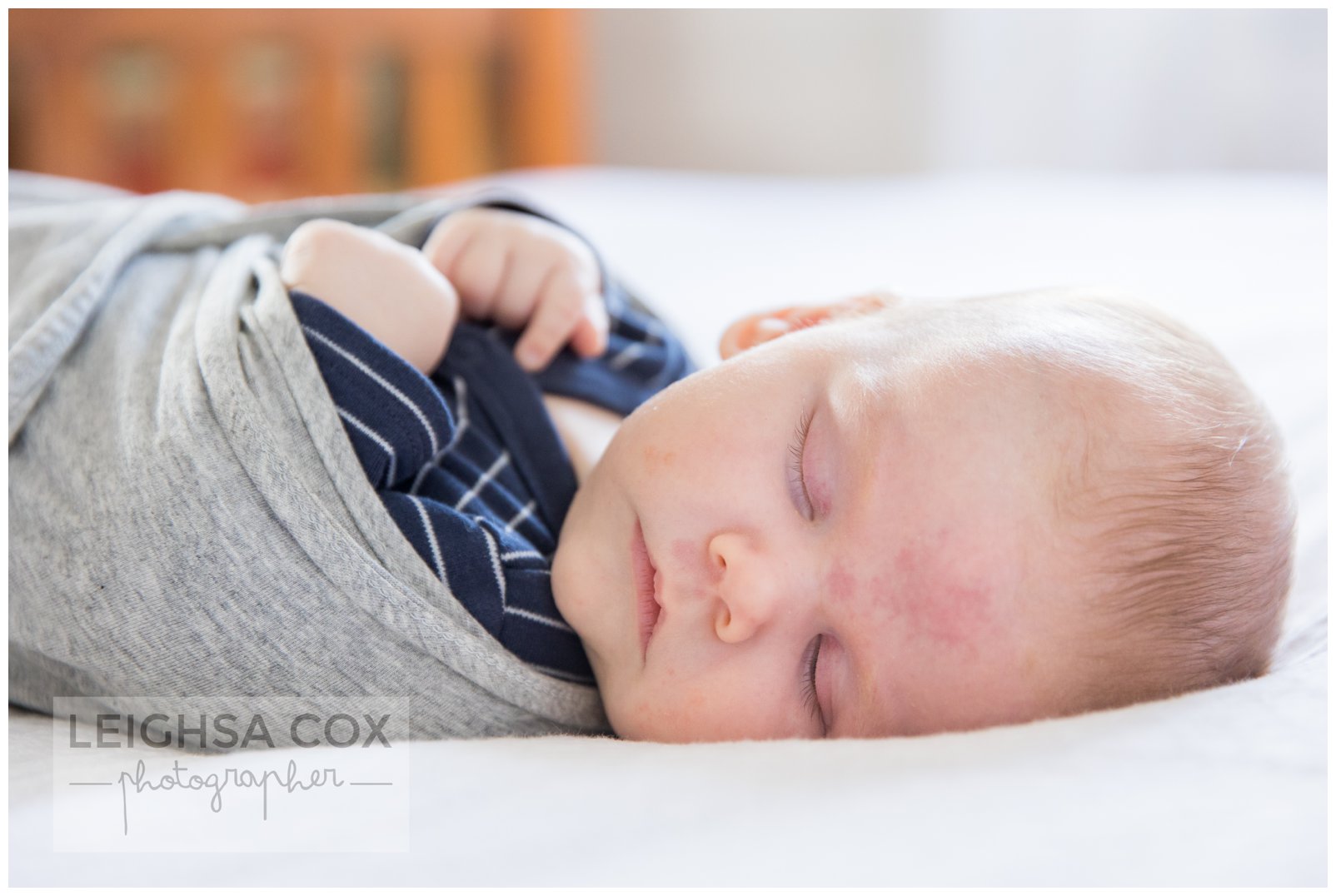 Portrait of newborn baby sleeping peacefully in swaddle surrounded by soft light fabric.